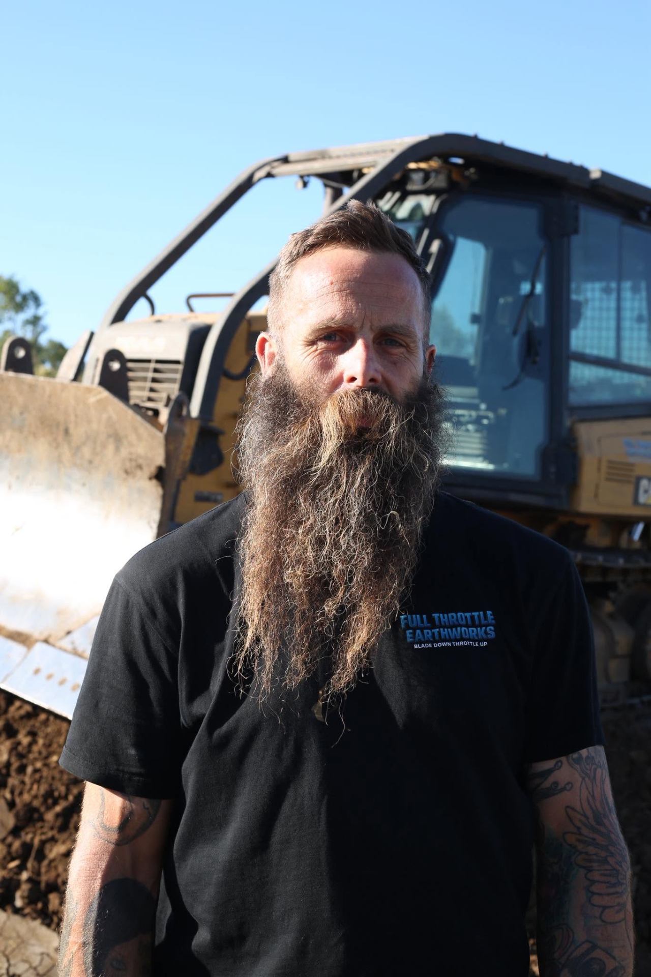 Adam Thurrowgood in a Full Throttle Earthworks shirt in front of his dozer on site