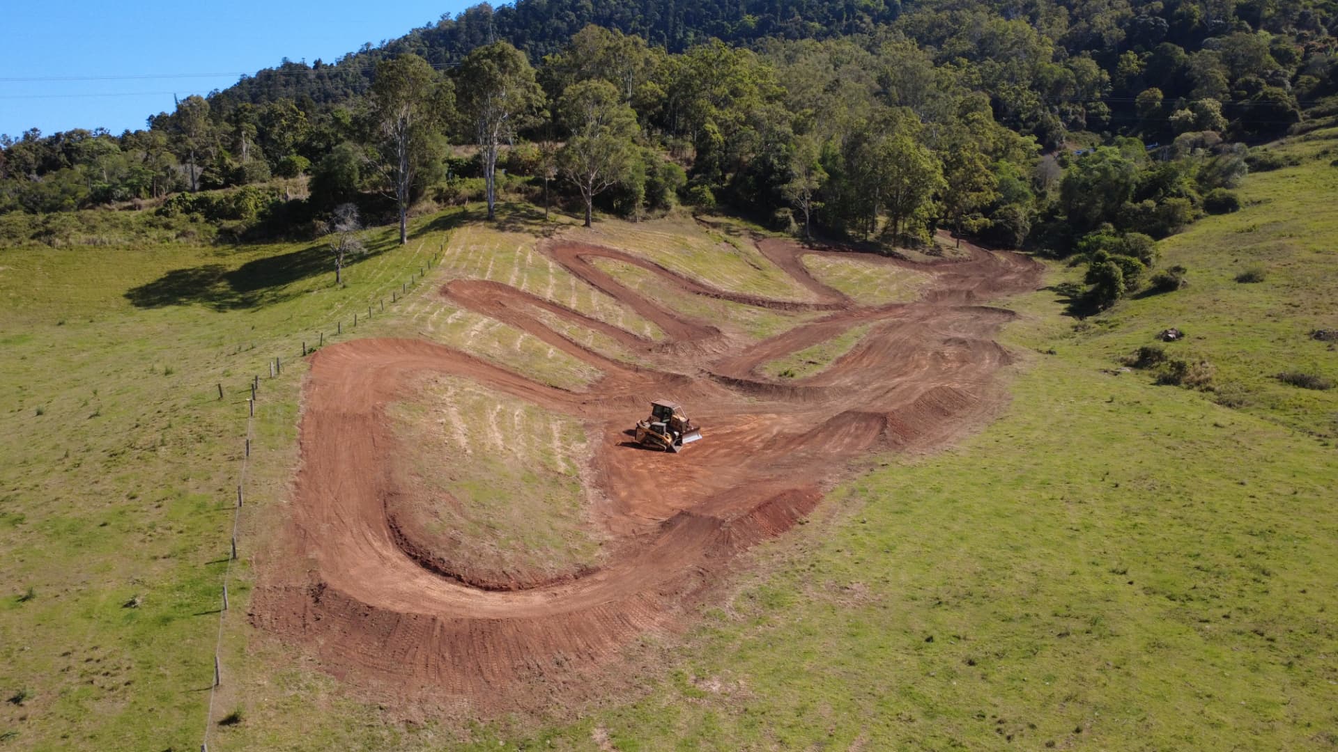 Aerial view of a motocross track under construction in green Australian countryside with a dozer shaping the ground
